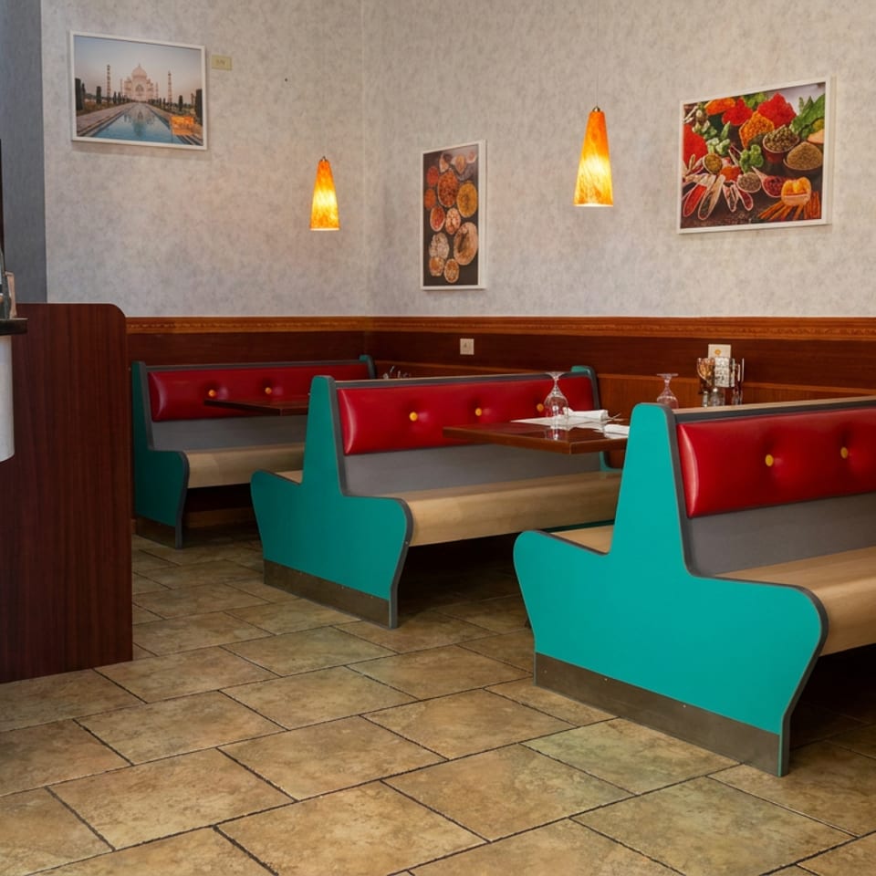 Colorful restaurant dining room with turquoise and red booths, set tables, pendant lights, food artwork, and a curved reception counter.
