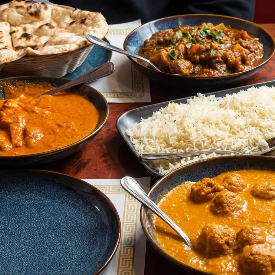 Indian restaurant spread with naan, basmati rice, and three bowls of creamy and spiced curries on a wooden table.