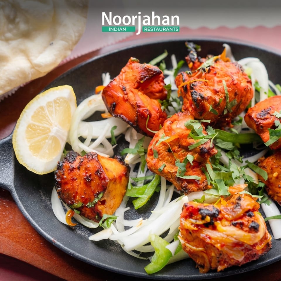 Tandoori chicken pieces garnished with cilantro and lemon on a black skillet, served with naan at Nooriahan Indian Restaurants.