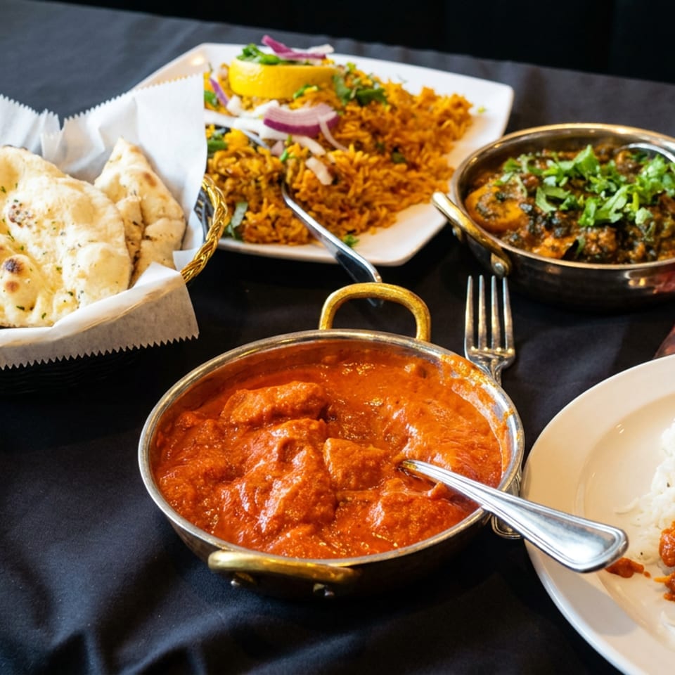 Indian restaurant spread with naan, rice, orange curry, lentil dish, garnished vegetables, water, and Coca-Cola on a dark table.